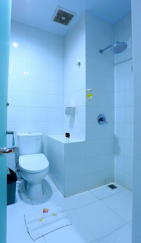 A bathroom with a toilet, a shower, and a towel on the floor. - Fizz Hotel Lombok (Mataram)