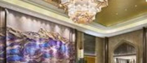 A spacious lobby with a large chandelier, a mural on the wall, and a reception desk.