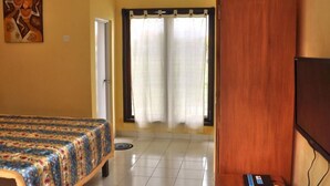 Habitación de hotel con cama, televisor, puerta y ventana con cortinas.