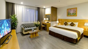 A hotel room with a bed, a sofa, a desk, a TV, and a plant. - London Hanoi Hotel (Hanoi)