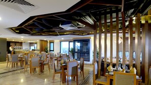 A spacious hotel dining area with multiple tables and chairs, a bar in the background, and large windows offering views. - London Hanoi Hotel (Hanoi)
