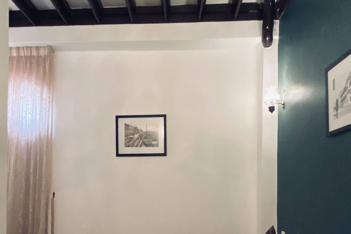 A neatly made bed with white and red bedding, a framed picture on the wall, and a window with curtains.