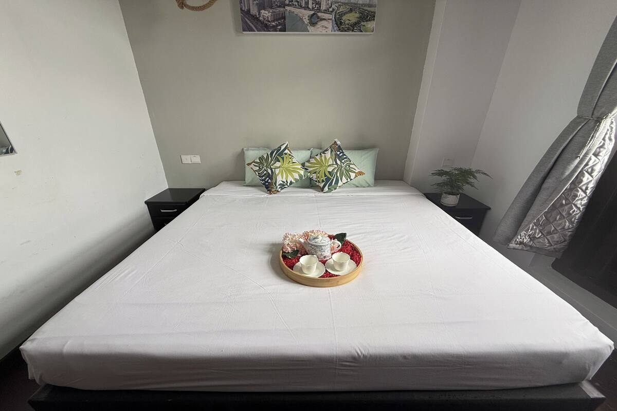 A neatly made bed with a tray of tea set and decorative pillows.