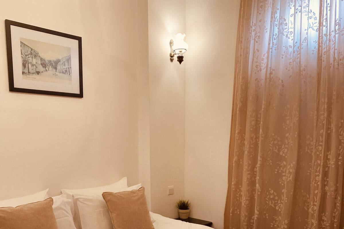 A neatly made bed with a red blanket, white pillows, and a framed picture on the wall.