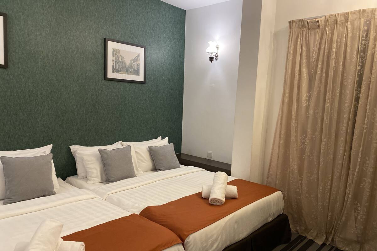 A hotel room with two beds, green walls, a framed picture, a wall-mounted light, and a curtain.
