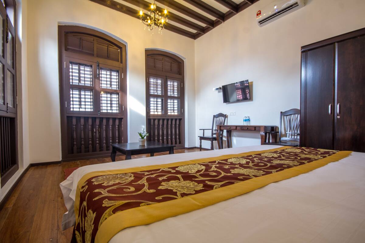 A hotel room with a large bed, wooden furniture, a chandelier, and a television on the wall.
