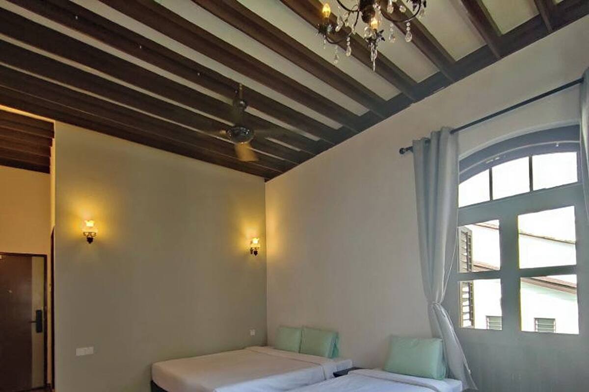 A room with two beds, wooden flooring, a chandelier, and a window with curtains.