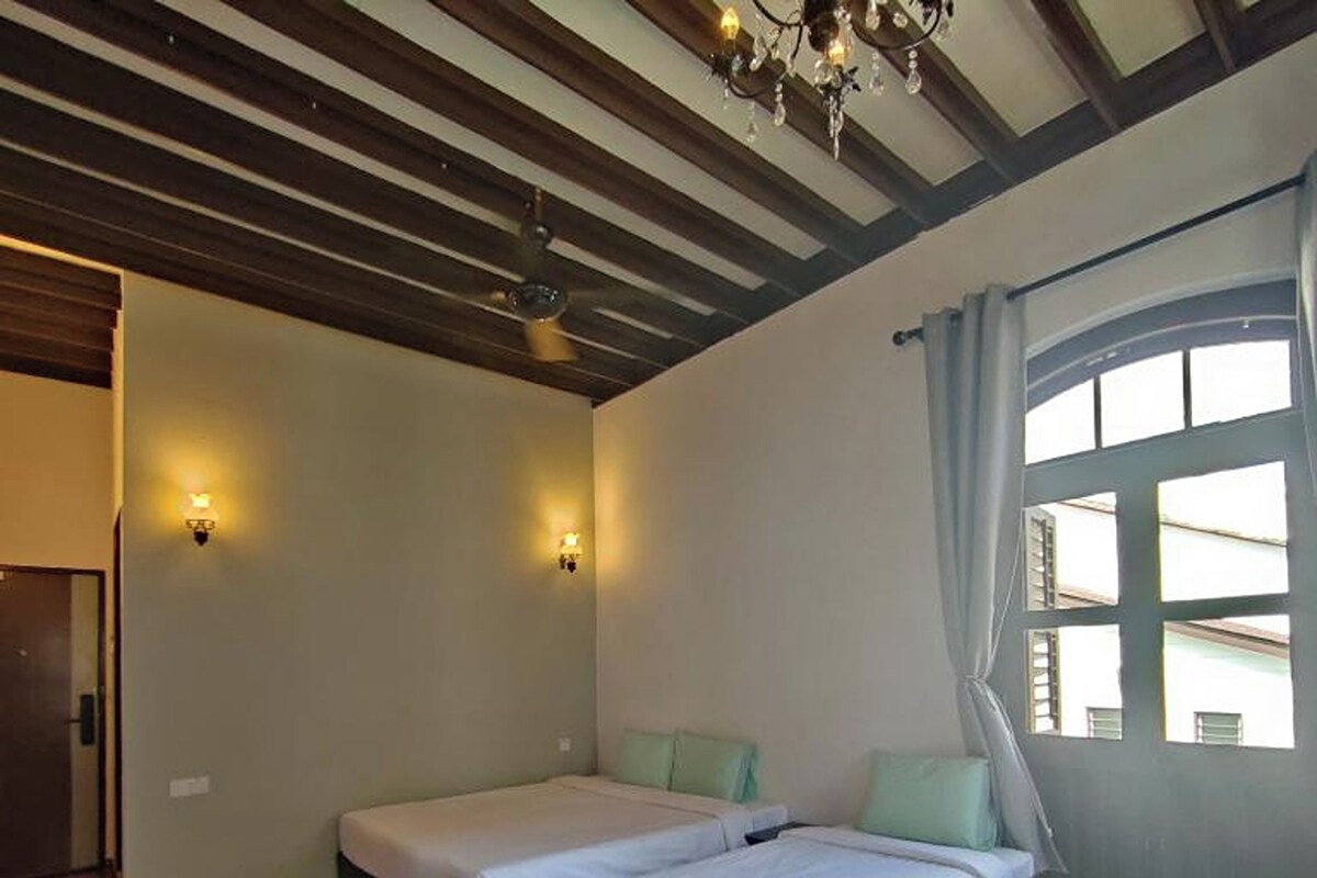 A room with two beds, wooden flooring, a chandelier, and a window with curtains.
