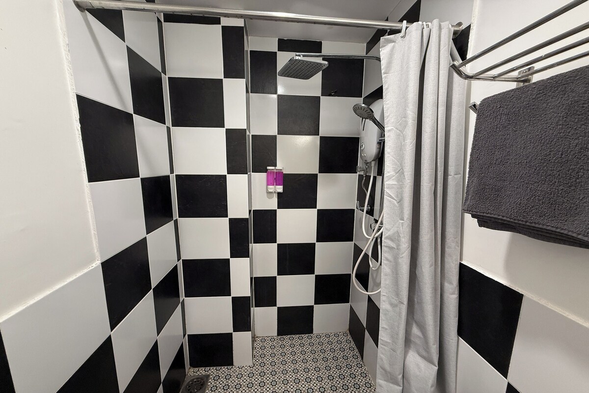 A bathroom with black and white checkered tiles, a shower with a handheld showerhead, and a towel rack with a towel.