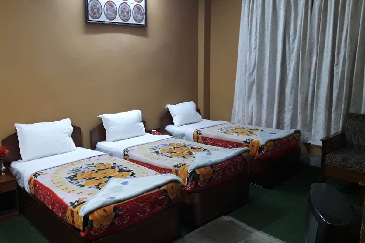 A hotel room with three single beds, each with a floral bedspread, white pillows, and a small table with a vase.