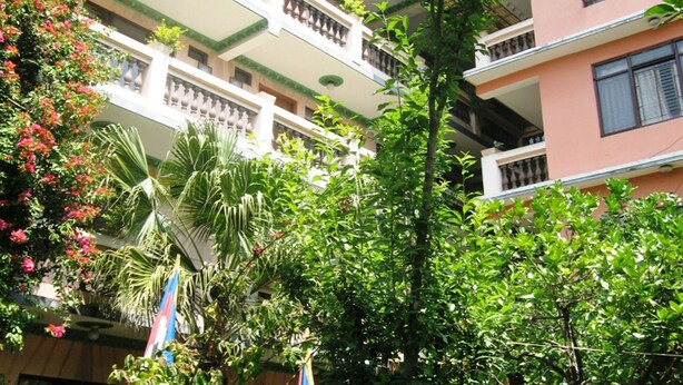Un edificio de varios pisos con balcones, rodeado de abundante vegetación y diversas plantas.