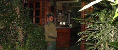 A man in uniform standing at a doorway with ornate wooden architecture and lush greenery.