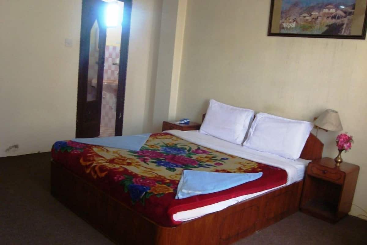 A bed with a floral bedspread, a bedside table with a lamp, and a wall-mounted picture.