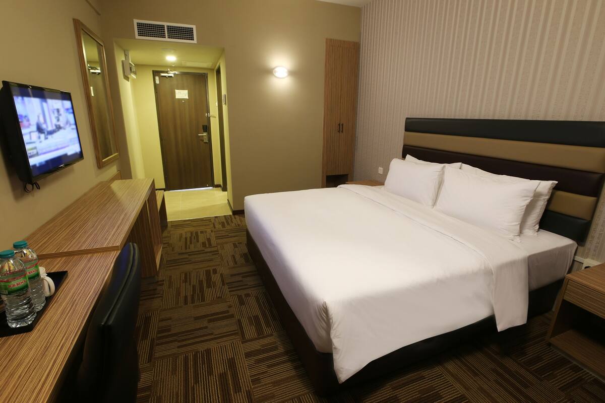 A hotel room with a bed, a desk with a television, a wardrobe, and a bathroom door.