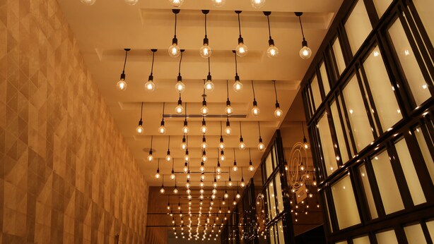 Un couloir avec des luminaires suspendus et de grandes fenêtres aux montures sombres.
