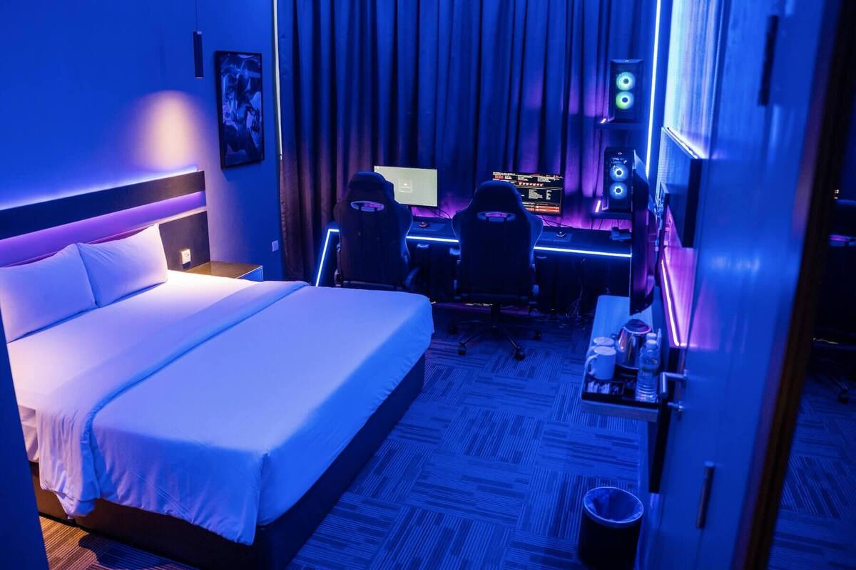 A hotel room with a large bed, a desk with a computer, two chairs, and a TV.