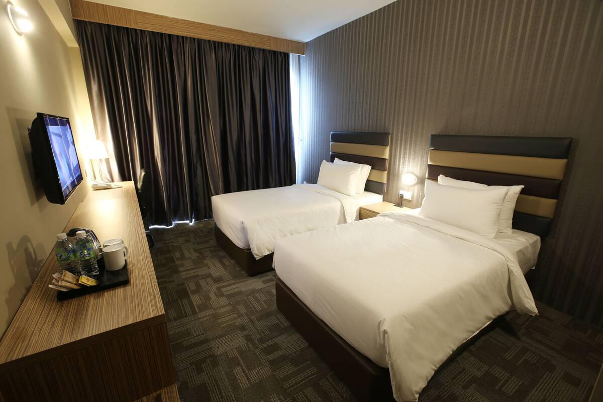 A hotel room with two beds, a desk with a TV, and a window with curtains.