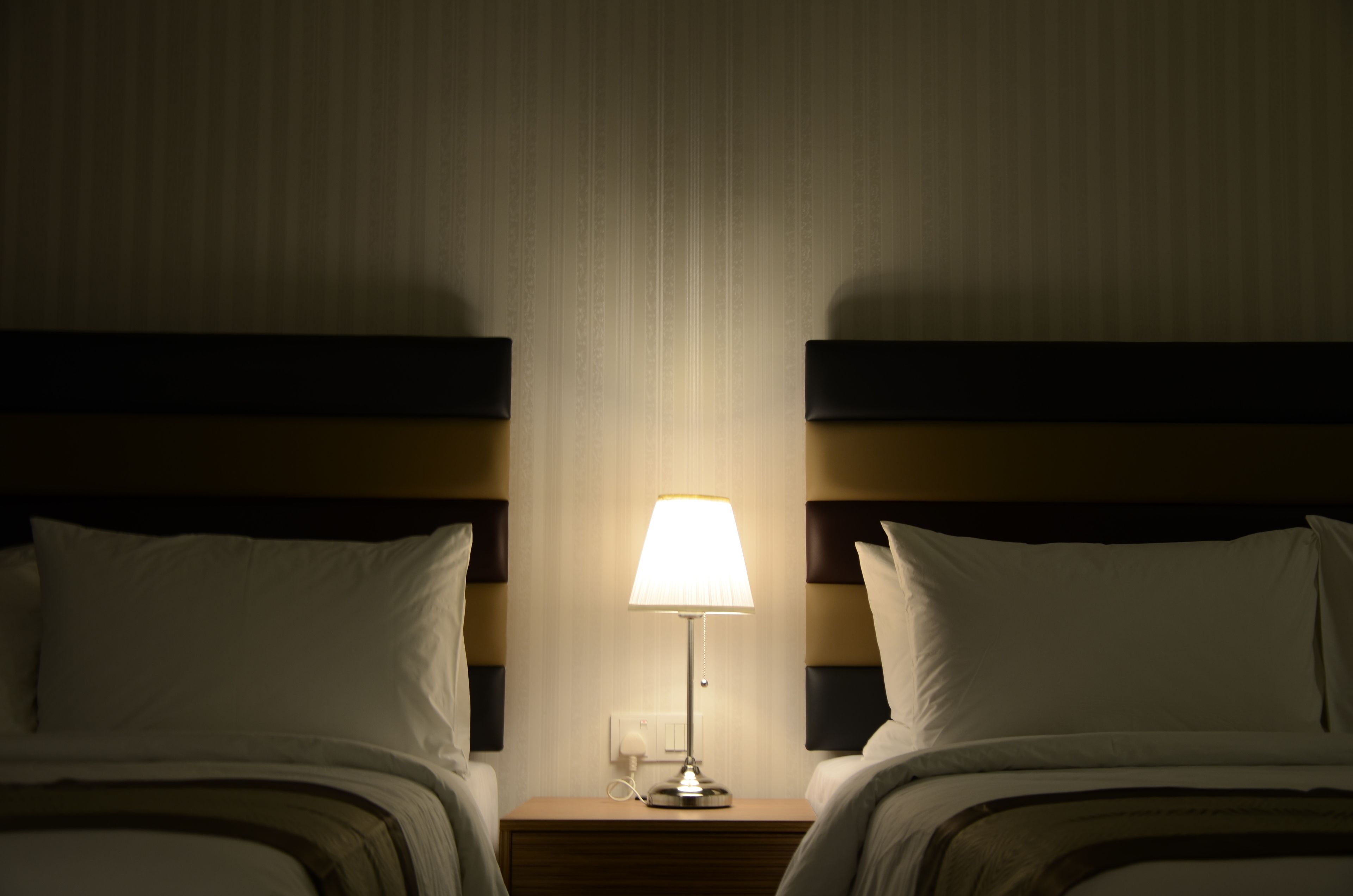 Habitación de hotel con dos camas, una mesita de noche con lámpara y un enchufe en la pared.