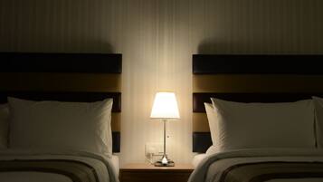 Habitación de hotel con dos camas, una mesita de noche con lámpara y un enchufe en la pared.