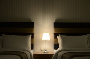 Habitación de hotel con dos camas, una mesita de noche con lámpara y un enchufe en la pared.