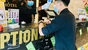 Un espace d’accueil d’hôtel comprenant un comptoir d’enregistrement, un thermomètre numérique pour vérifier la température et un panneau indiquant les mesures à prendre lors de l’enregistrement, conformément aux protocoles sanitaires.
