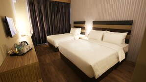 Une chambre d’hôtel avec deux lits, un bureau en bois sur lequel se trouve un plateau avec des articles de toilette, et un téléviseur fixé au mur.