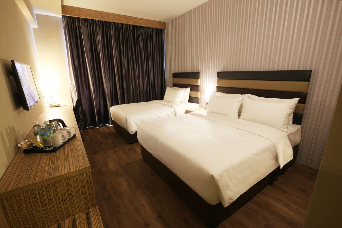 A hotel room with two beds, a wooden desk with a tray of toiletries, and a TV mounted on the wall.