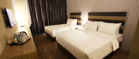 A hotel room with two beds, a wooden desk with a tray of toiletries, and a TV mounted on the wall.
