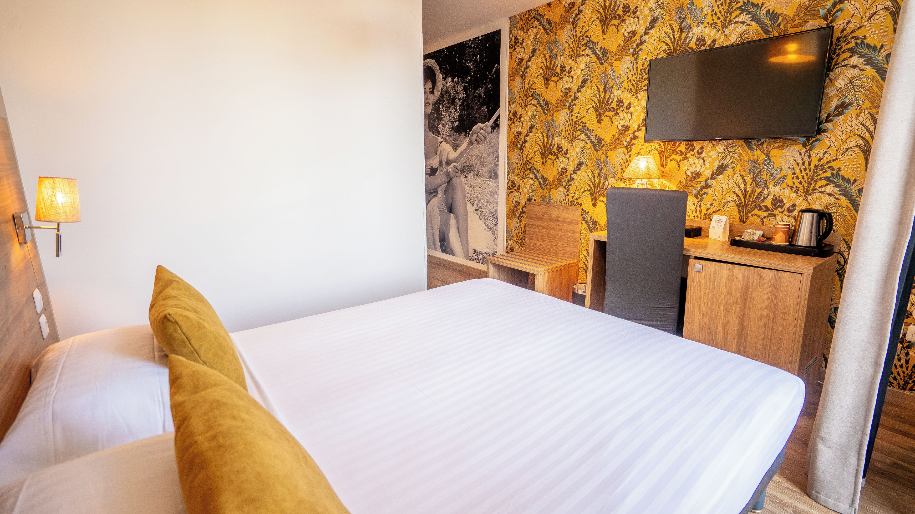 A hotel room with a bed, a desk, a chair, a flat-screen TV, and a lamp.