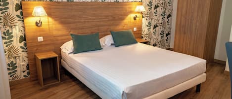 A neatly made bed with two pillows, a wooden headboard, two bedside lamps, and a small wooden nightstand.