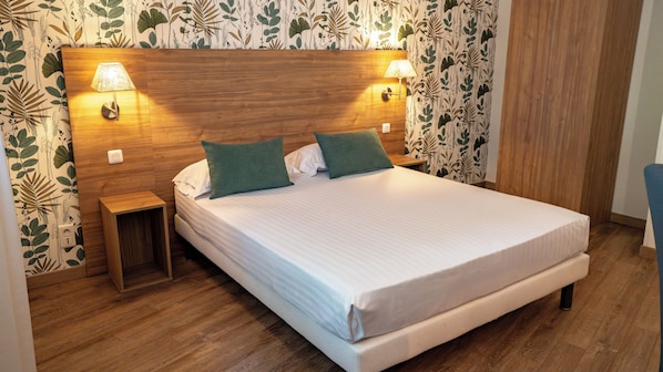 Cama bem arrumada com duas almofadas, cabeceira de madeira, duas luminárias de mesa e um criado-mudo de madeira.