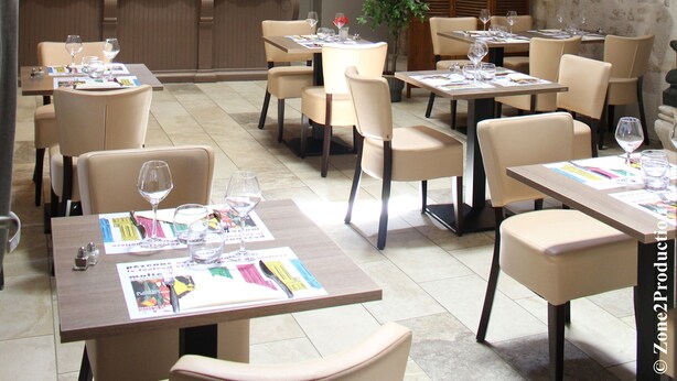 Ein Restaurant mit mehreren Tischen, Stühlen, einer Bar und einem Balkon mit schmiedeeisernem Geländer.
