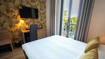 A hotel room with a bed, a desk, a chair, a TV mounted on the wall, and a balcony with a view.