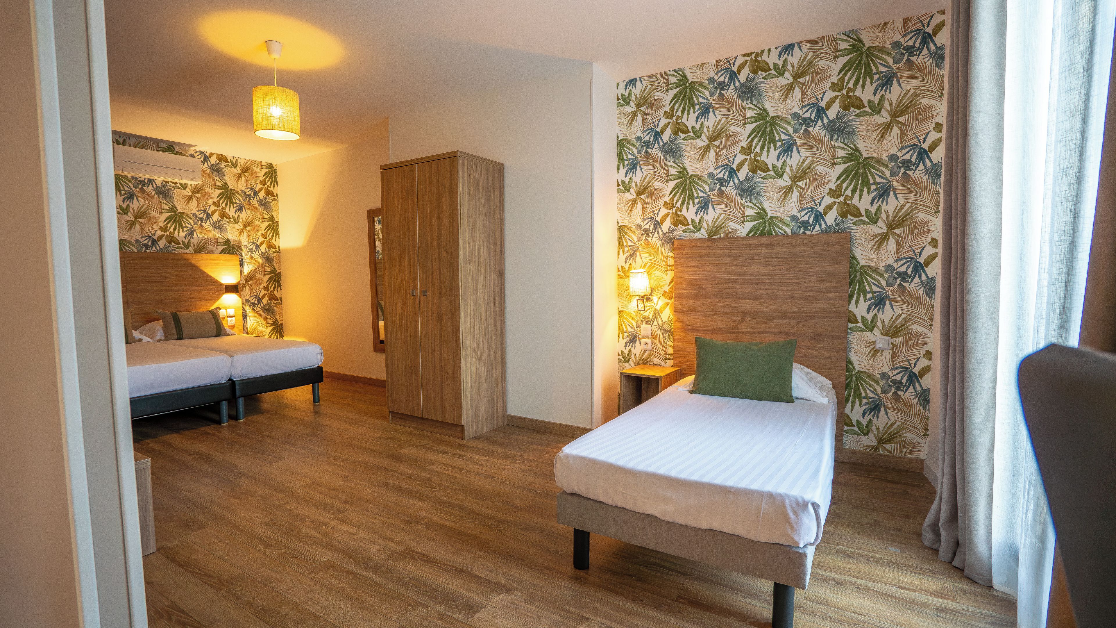 Une chambre d’hôtel comprenant un lit, une table de chevet, une armoire et un mur orné d’un motif de feuilles tropicales.