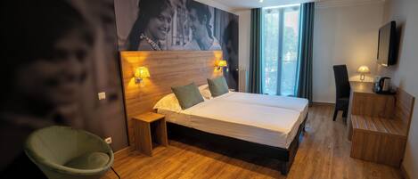 Een hotelkamer met een groot bed, nachtlampen, een stoel, een bureau en een televisie.