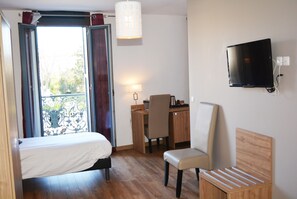 Une chambre d’hôtel avec un lit, un bureau, une chaise, une télévision et un balcon avec des rideaux.