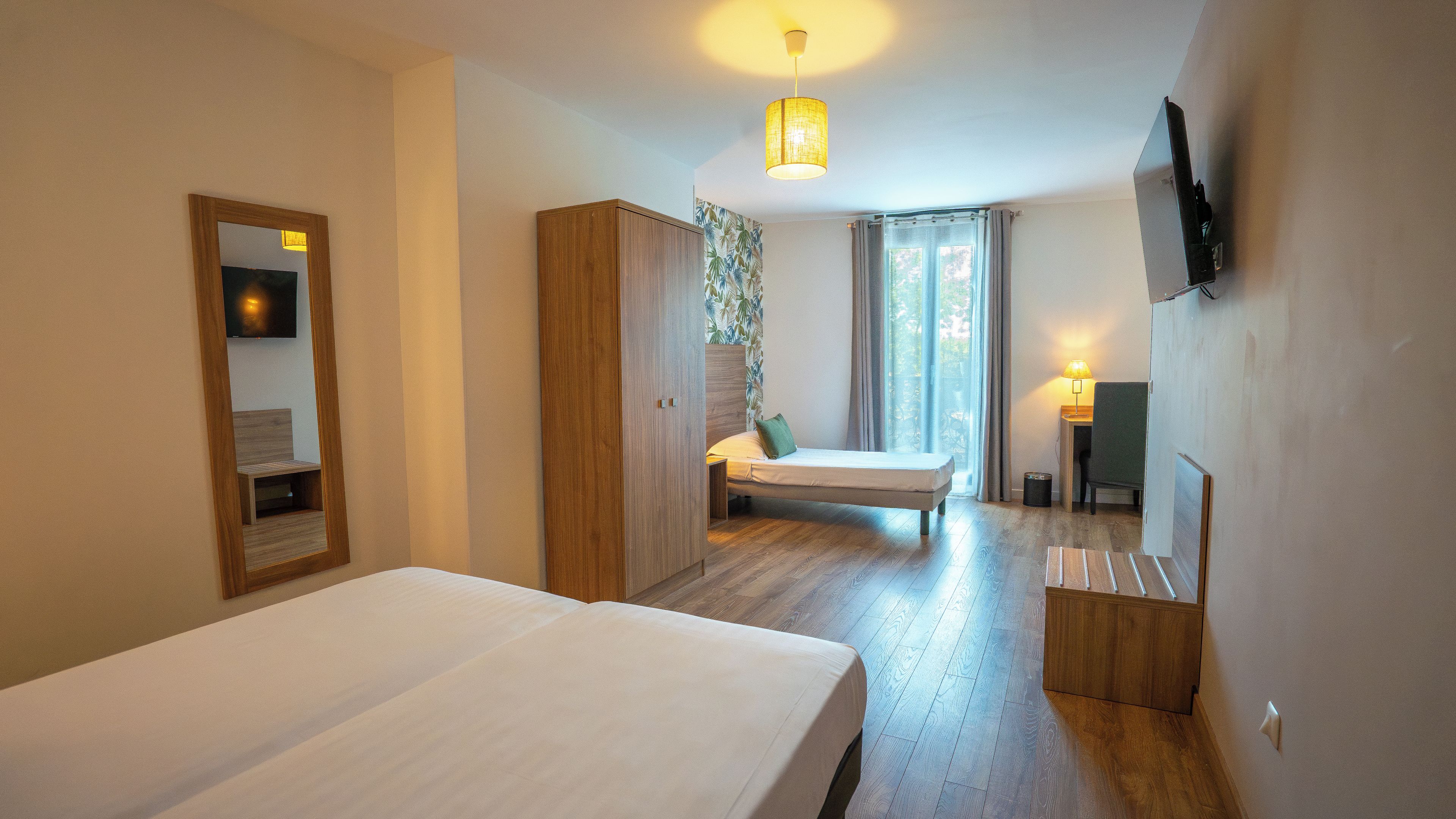A hotel room with a bed, a desk, a chair, a television, and a window with curtains.