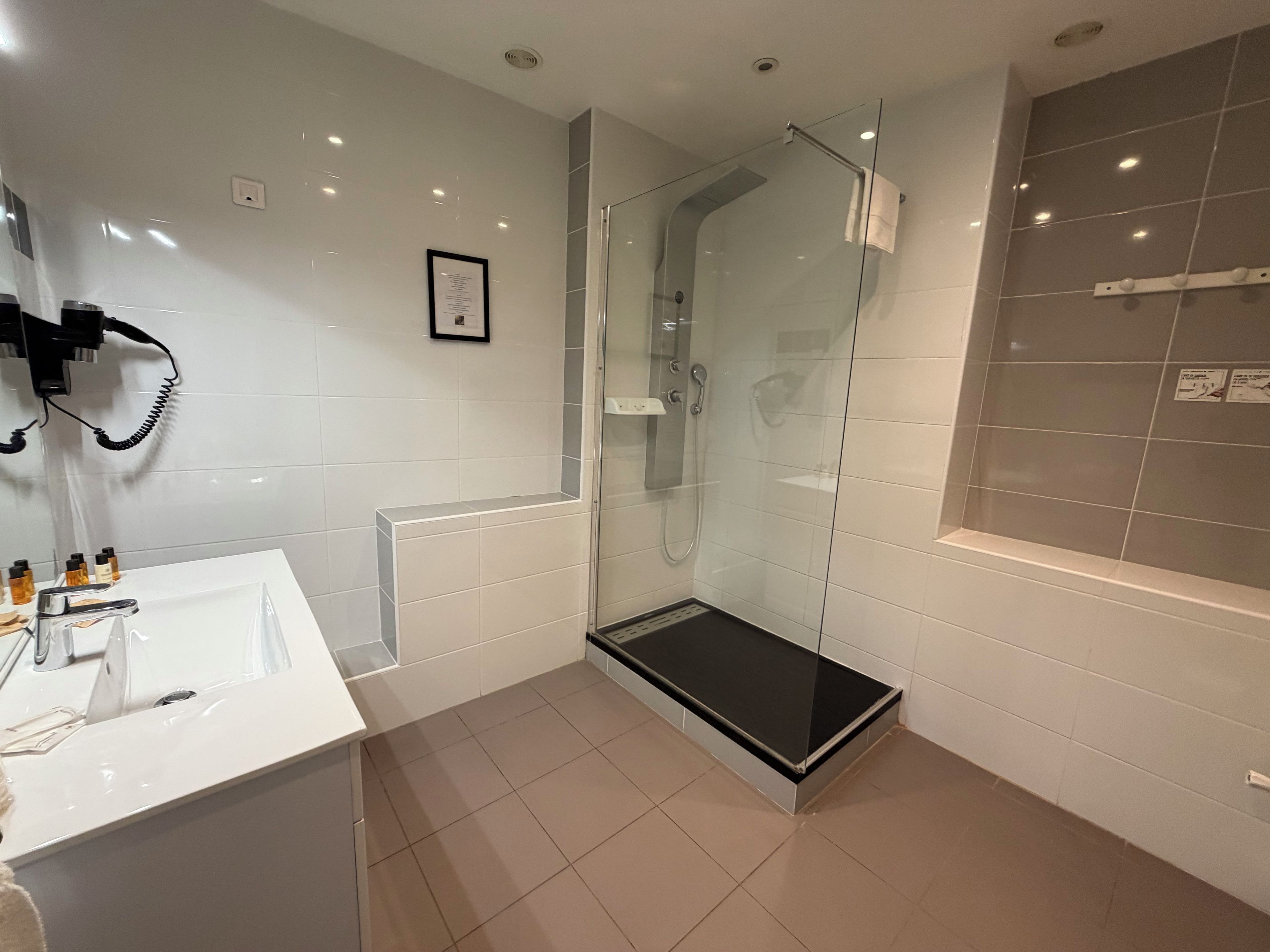 Een moderne badkamer met een glazen douchecabine, een wit wastafelmeubel met spiegel en een betegelde vloer.