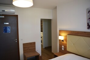 Une chambre d’hôtel avec un lit en bois, une table de chevet avec une lampe, une petite chaise en bois et une porte avec une pancarte.