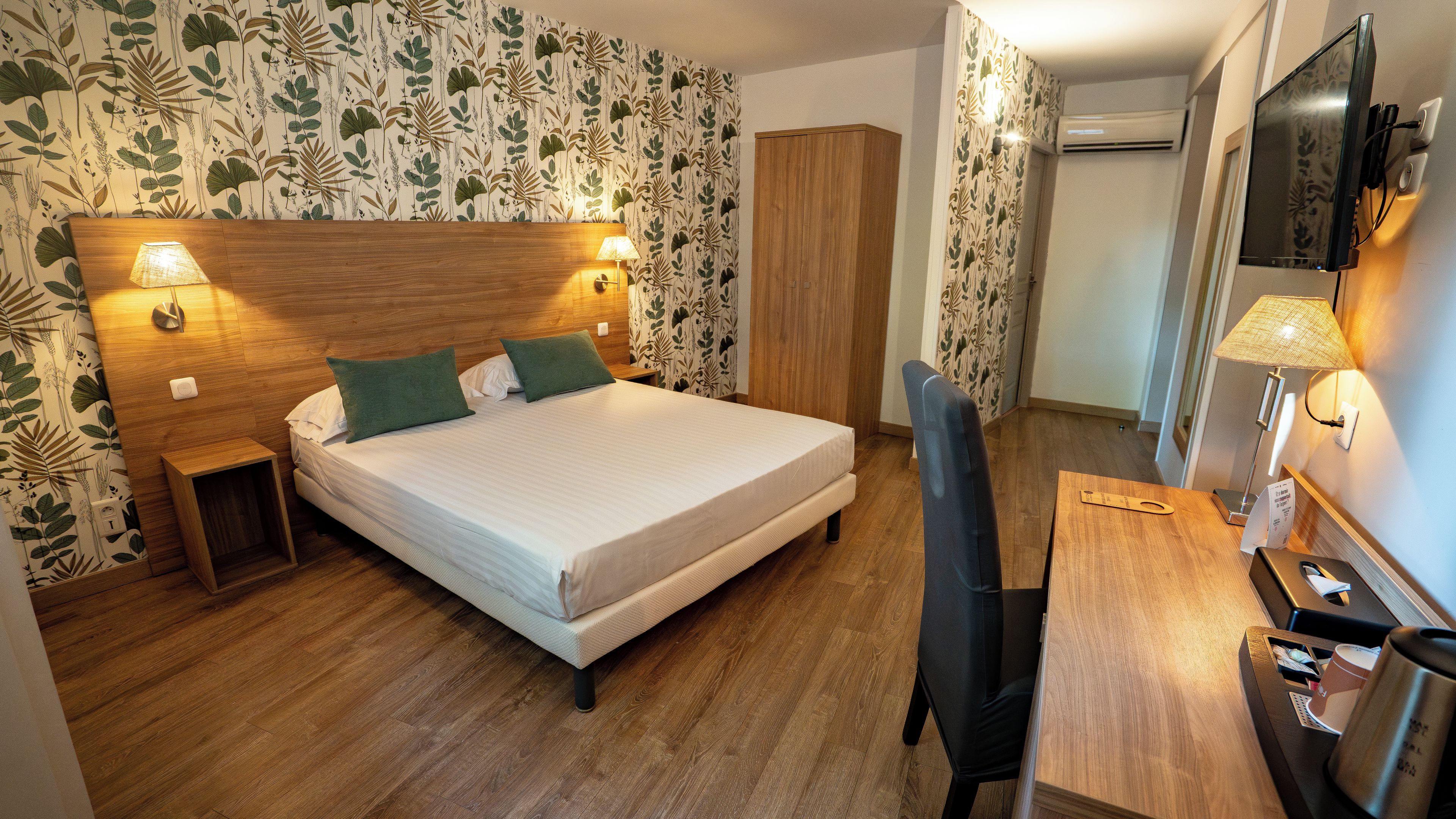 Habitación de hotel con cama, lámparas de noche, escritorio con silla y televisión.