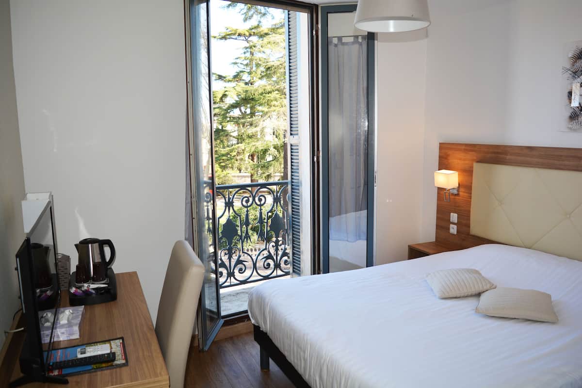 A hotel room with a bed, a desk with a computer, a coffee maker, and a view of the outdoors.