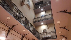 Ein mehrgeschossiges Interieur mit schmiedeeisernem Balkongeländer, Pendelleuchten und einer Steinwand.