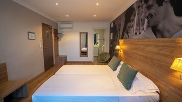 Habitación de hotel con cama doble, cabecera de madera, una silla, un espejo y aire acondicionado de pared.