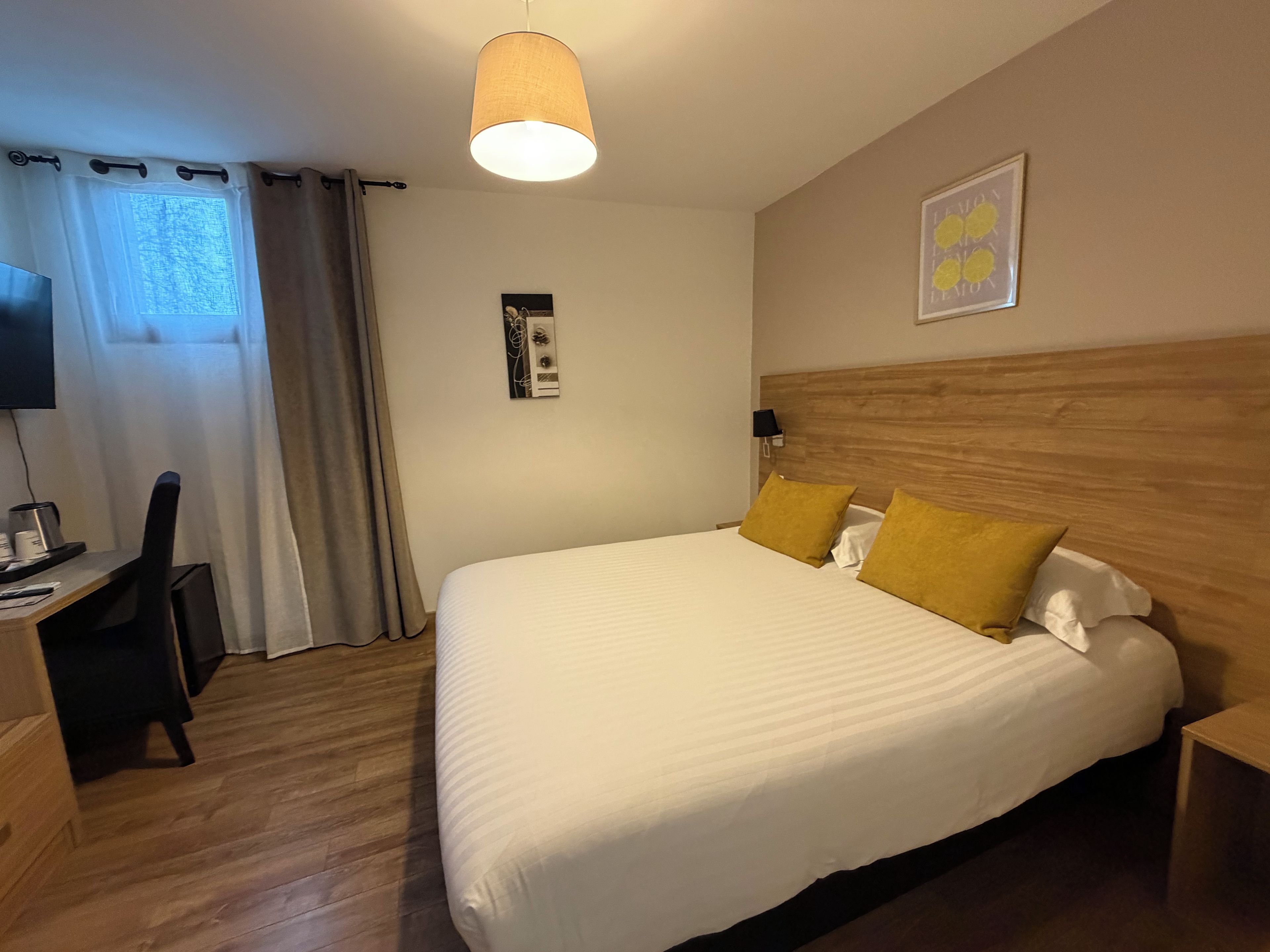 Une chambre d’hôtel équipée d’un lit, d’un bureau, d’une chaise, d’une télévision et d’une fenêtre avec des rideaux.