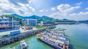 A waterfront area with a large fishing boat docked at a pier, buildings in the background, and mountains in the distance. - Sea Star Hostel Yeosu (Yeosu)
