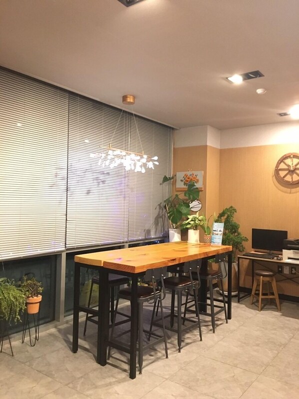A room with a wooden table and chairs, a computer desk with a monitor, keyboard, and printer, and a wall with a clock and a decorative wheel. - Sea Star Hostel Yeosu (Yeosu)