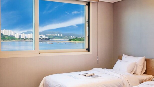 A hotel room with a large window offering a view of a cityscape and water. - Sea Star Hostel Yeosu (Yeosu)