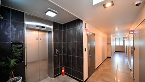 A hotel corridor with two elevators, a fire extinguisher, and a potted plant. - Sea Star Hostel Yeosu (Yeosu)