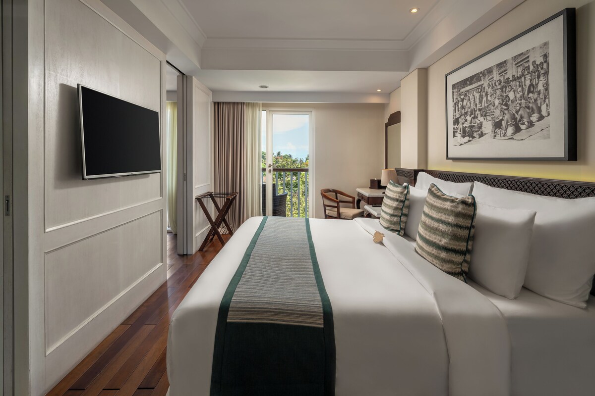 A hotel room with a large bed, a flat-screen TV mounted on the wall, a balcony with a view, and a framed picture on the wall.