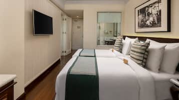 A hotel room with two beds, a flat-screen TV, a framed photo on the wall, and a bathroom visible through an open door.